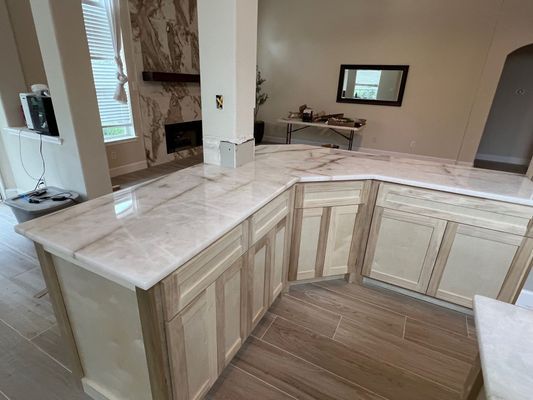 Light wood kitchen with marble countertops and a pass-through opening to a living room