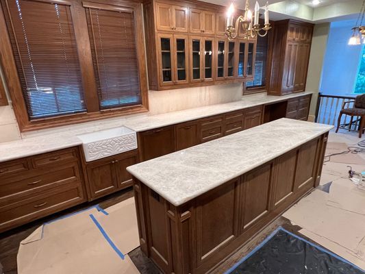 Wooden kitchen with central island, cream countertops, cabinets, and taped-off floor during renovation