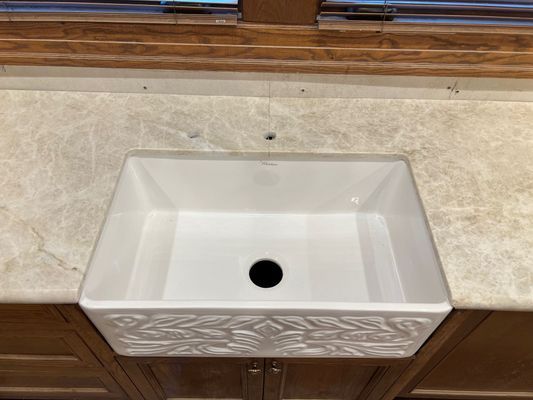 White vessel sink with black drain on a beige countertop against a tiled wall.