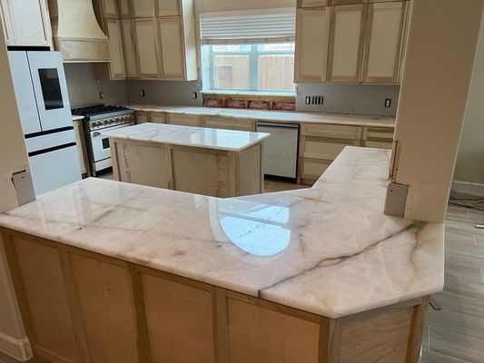 Bright kitchen with cream cabinets, marble countertops, island, and a large window above the sink.