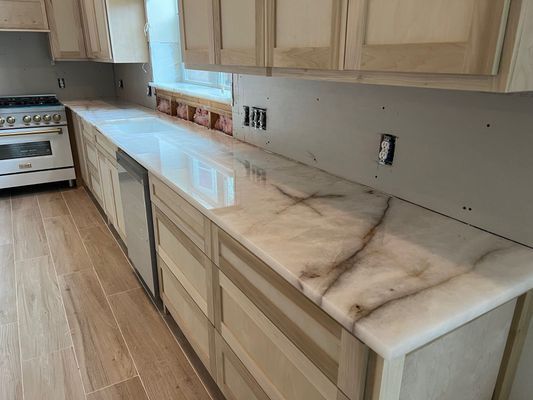 Empty kitchen with light wood cabinets, white marble countertops, and a stove on the left.