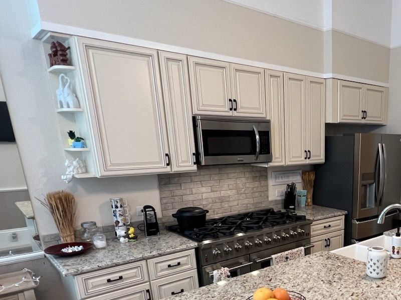 Modern kitchen with cream cabinets, black stove, stainless microwave, and granite countertops.