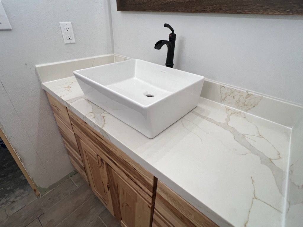 Modern bathroom vanity with white vessel sink, black faucet, and marble-look countertop