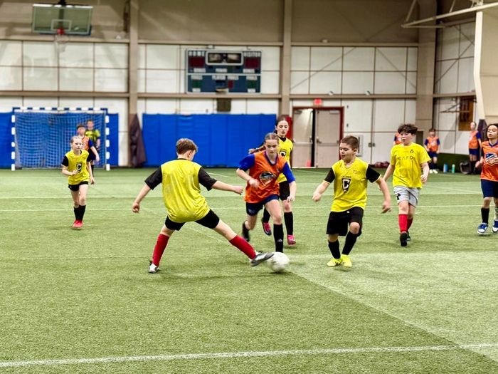 Youth soccer team holding a “Champions” banner in an indoor gym after an Adirondack Coast Sports win.