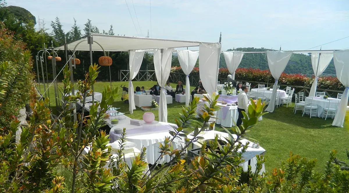 Evento all'aperto con tendoni drappeggiati di bianco e tavoli su un prato verde.