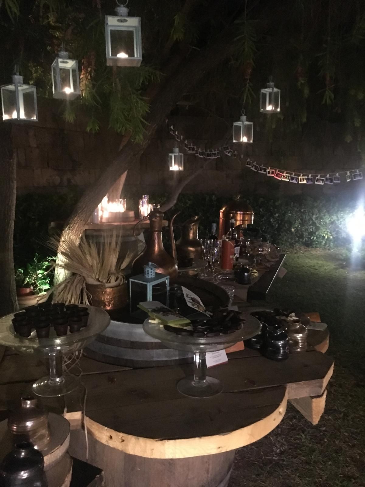 Tavolo da dessert all'aperto, lanterne appese a un albero, illuminate di notte.