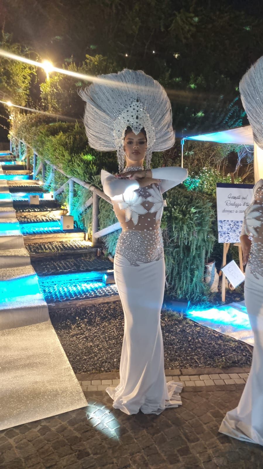 Donna in costume bianco con elaborato copricapo, in posa all'aperto di notte.