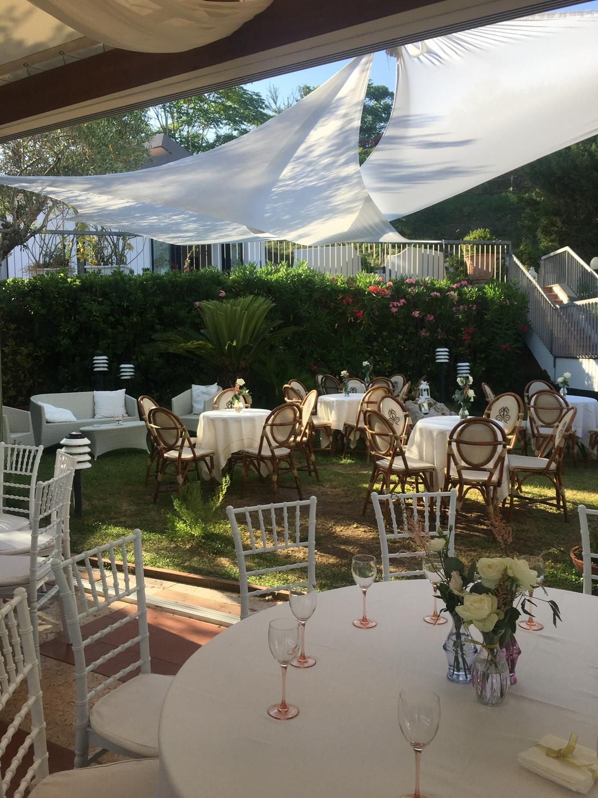 Allestimento per eventi all'aperto con tavoli e sedie sotto una tettoia bianca, giardino sullo sfondo.