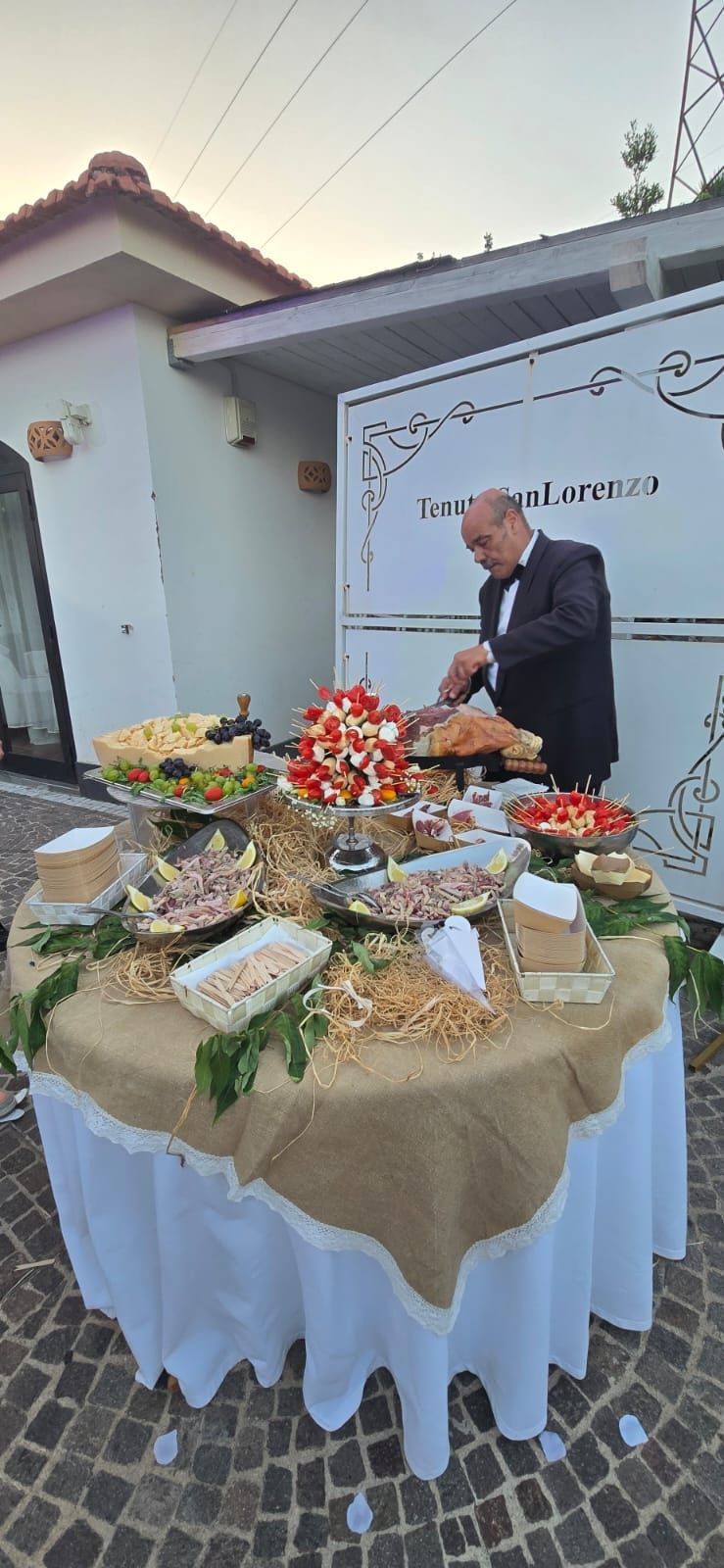Un uomo in smoking taglia la carne su un tavolo da buffet imbandito.
