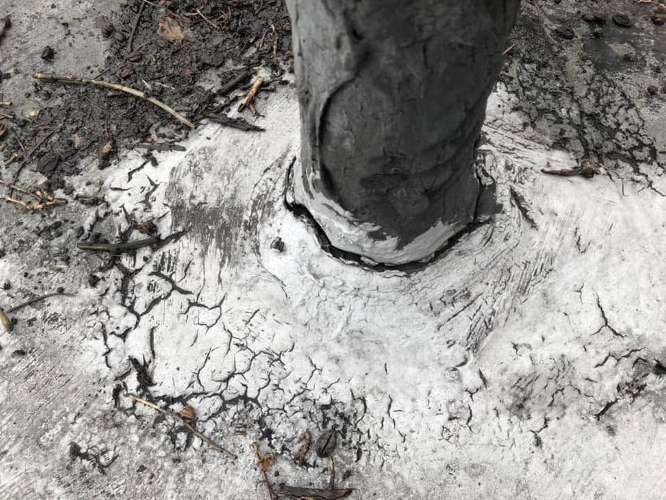 Cracked white paint or plaster around a gray metal pole set in dirt and debris