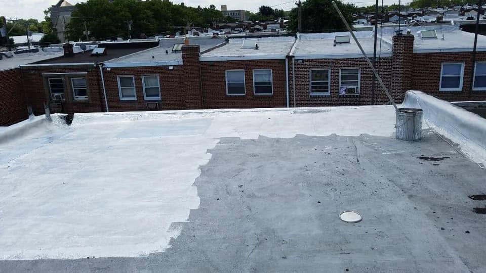 Flat rooftop with white roof coating, gray section, and brick buildings in the background.