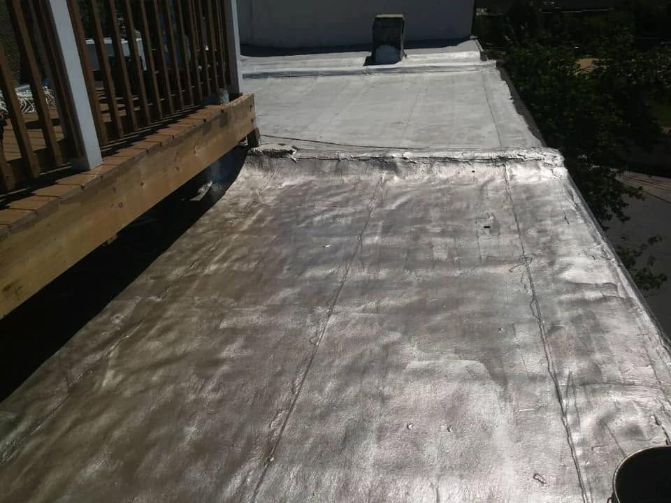 Weathered wooden deck leading to a concrete walkway beside a house and trees.