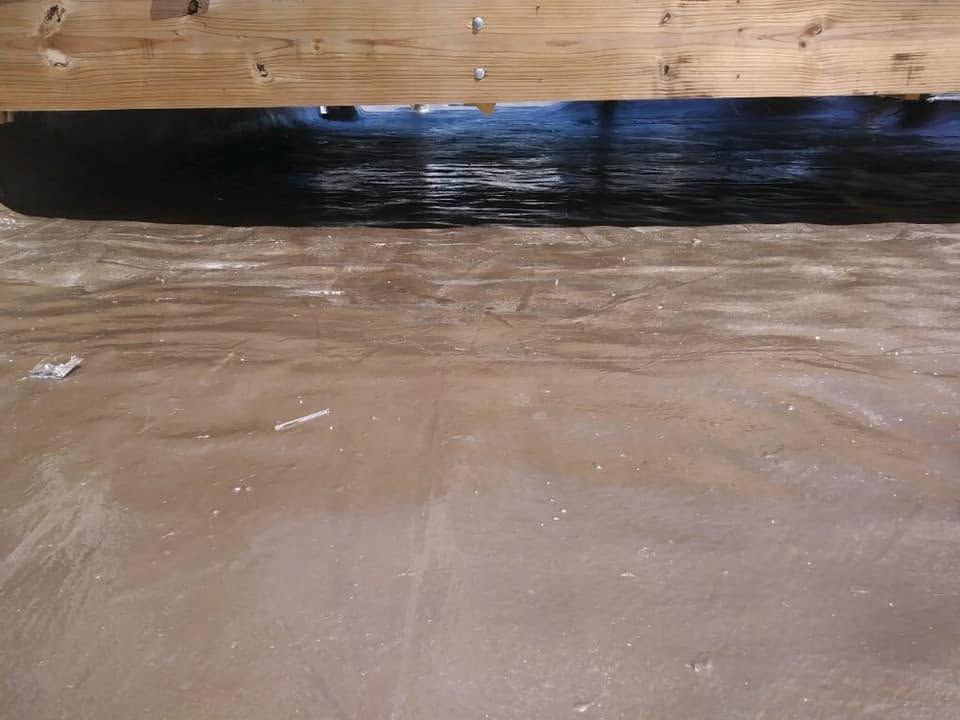 Fresh concrete floor with a black waterproofing strip along a wooden wall