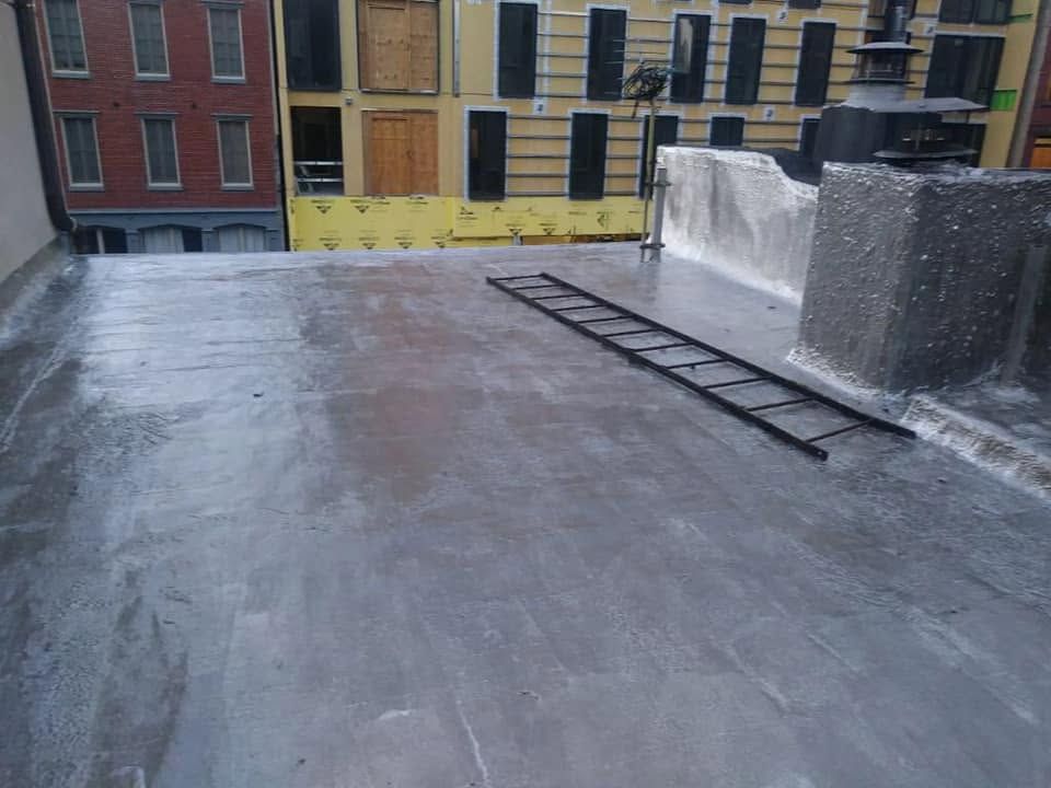 Rooftop with a ladder, gray surface, and brick buildings in the background