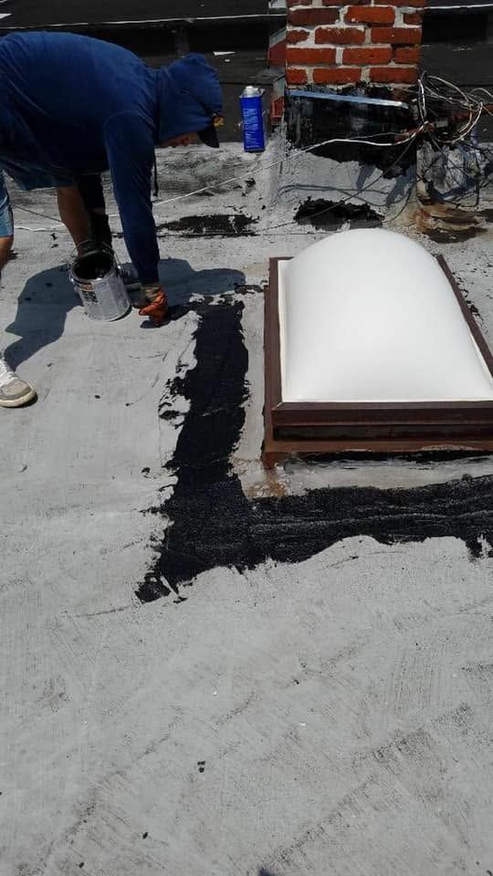 Person painting a rooftop around a white skylight dome with black waterproof coating