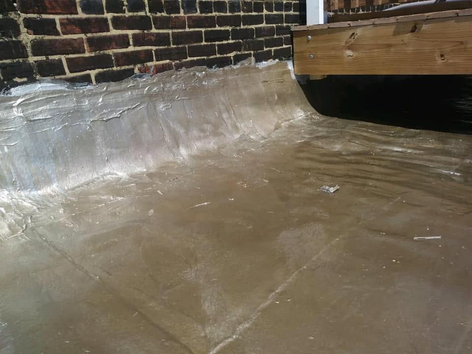 Transparent plastic sheeting covering a floor along a brick wall under a wooden beam.