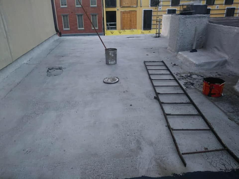 Rooftop with a ladder, small buckets, and a concrete surface near a wall and red doors.