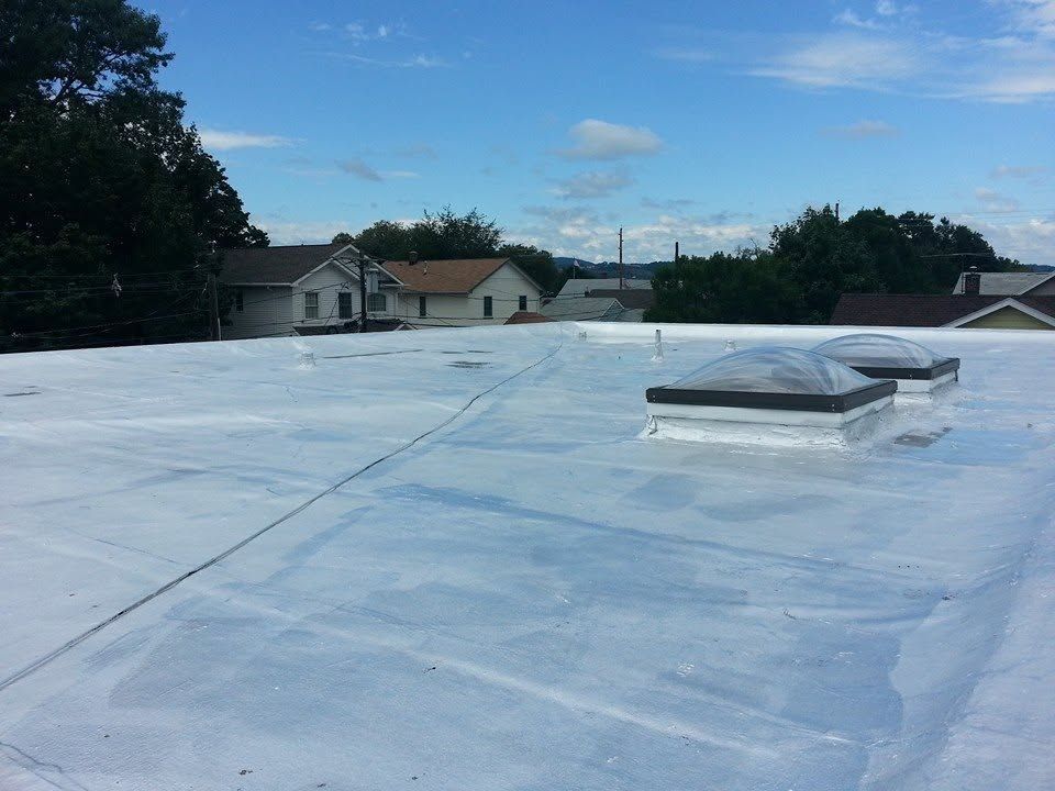 Flat white rooftop with a small skylight, trees and houses visible in the distance under a blue sky.