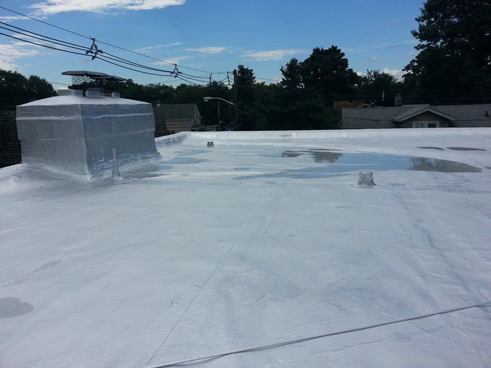 White-coated rooftop with HVAC units under a cloudy sky, viewed from above.
