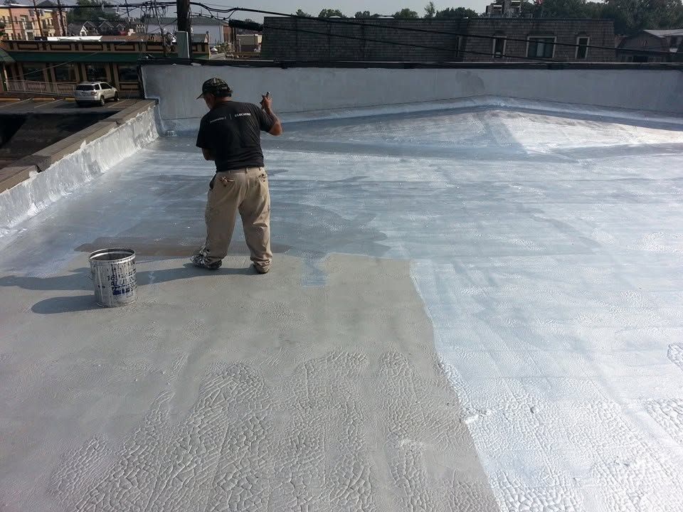Worker applying coating on a rooftop surface with a roller and bucket.