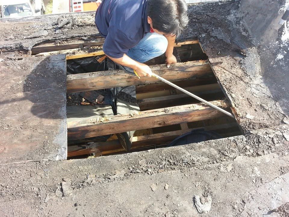 Worker inspecting damaged wooden beams in a hole on a rooftop.