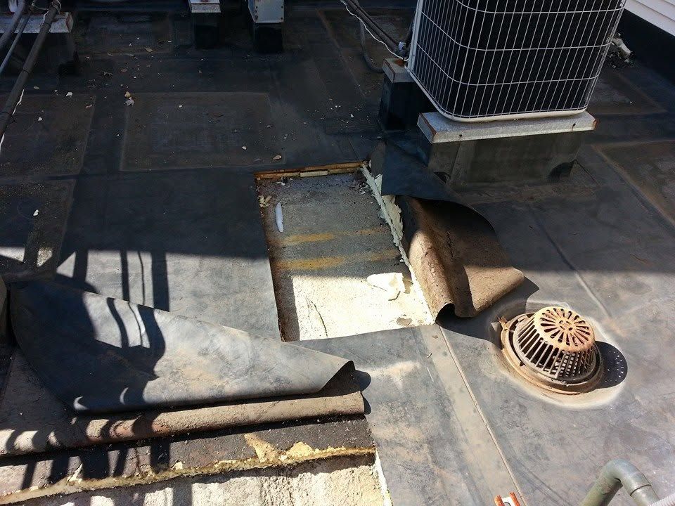 Damaged rooftop with torn tar paper, exposed insulation, and a rusted vent fan under an HVAC unit