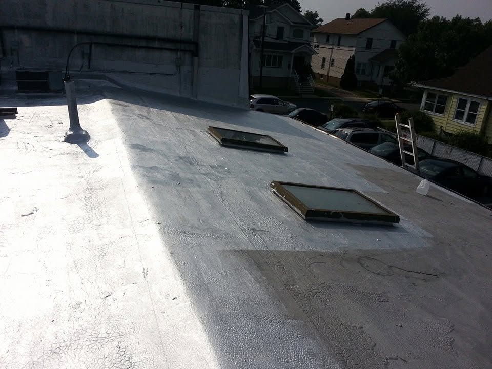 Flat rooftop with two skylights and a vent pipe in bright sunlight, buildings in the background