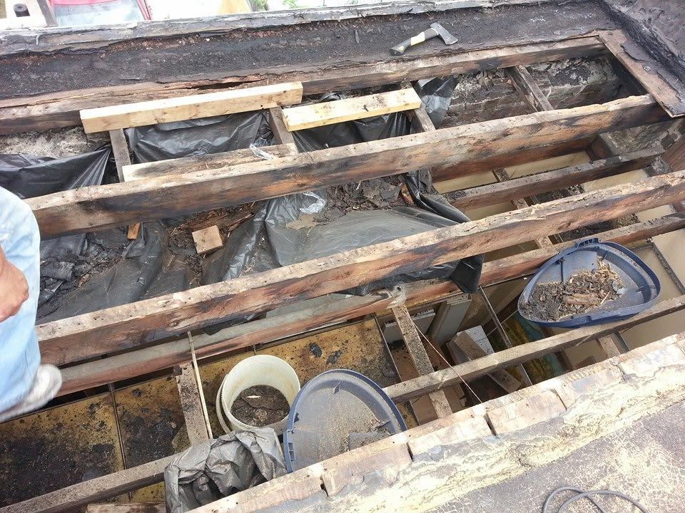 Wooden floor beams exposed during renovation, with buckets and tools visible below.