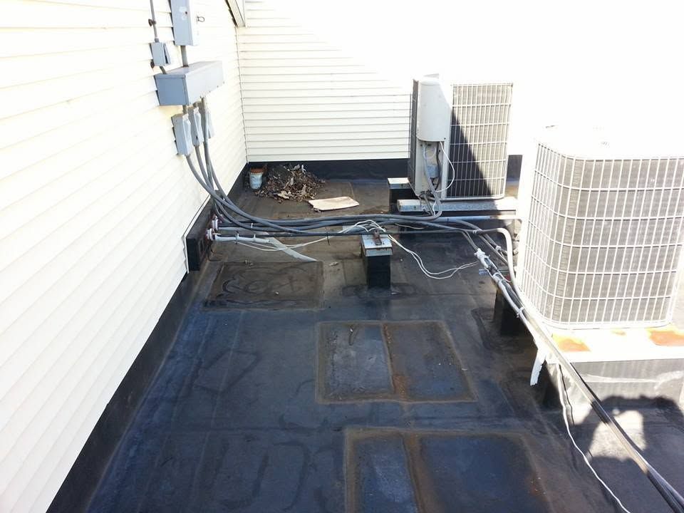 Outdoor HVAC units and exposed black tarp covering the ground beside a building wall