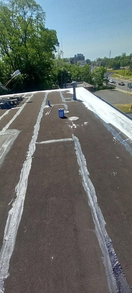 Flat rooftop with white sealant lines, surrounded by trees and a road on a sunny day
