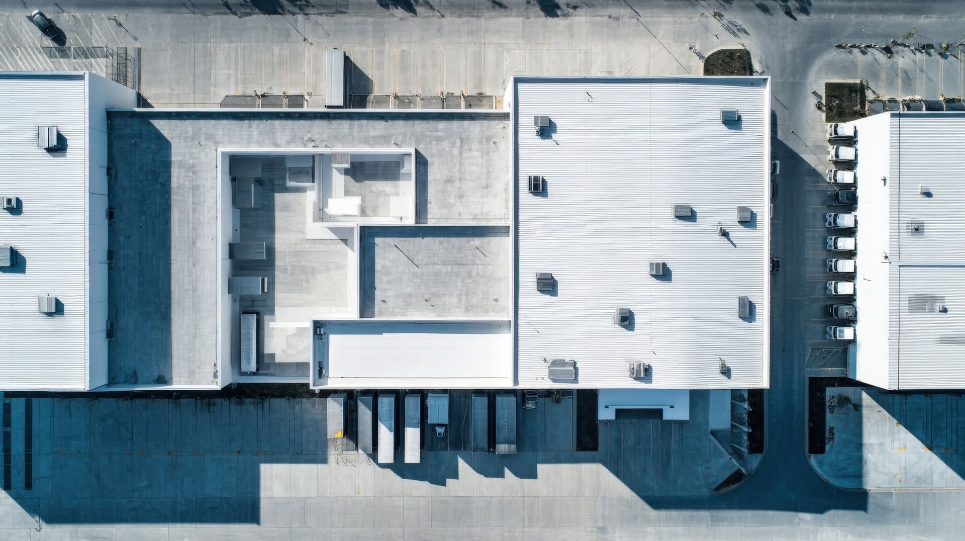 Aerial view of a flat-roofed industrial building with rooftop vents and long shadows.