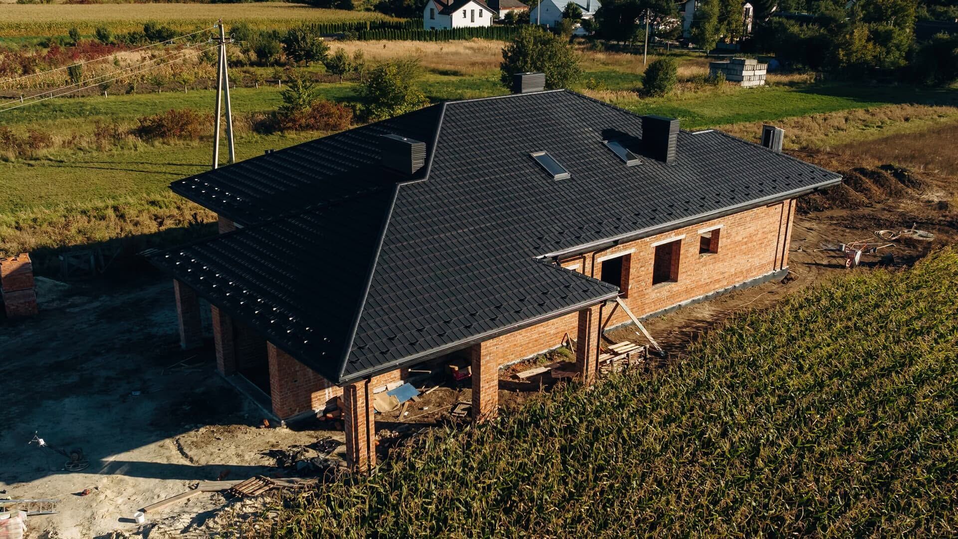 Aerial view of a newly built brick house with a dark roof in a rural field.