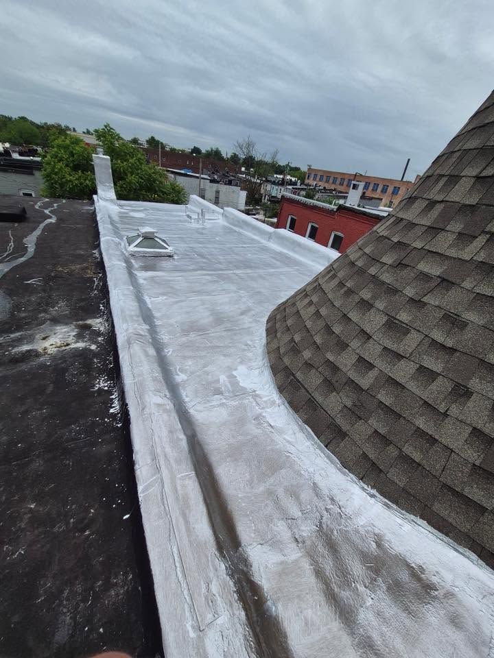 Rooftop with white waterproof coating beside dark shingles and a brick tower under an overcast sky