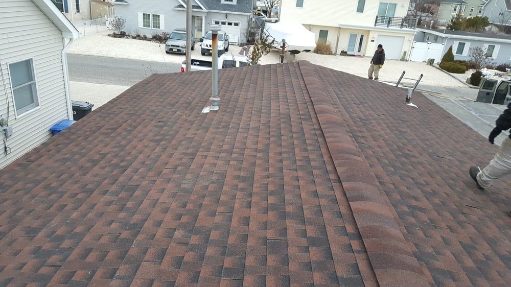Rooftop with brown shingle roofing and vents, viewed from above in a suburban neighborhood.