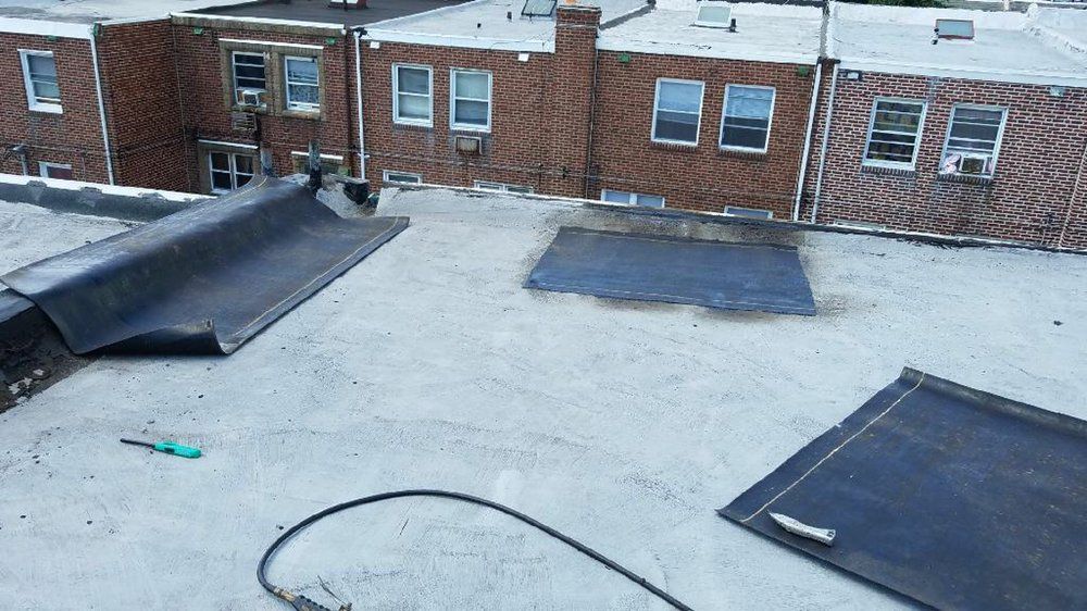 Rooftop with gray surface, black vents, and brick apartment buildings in the background.