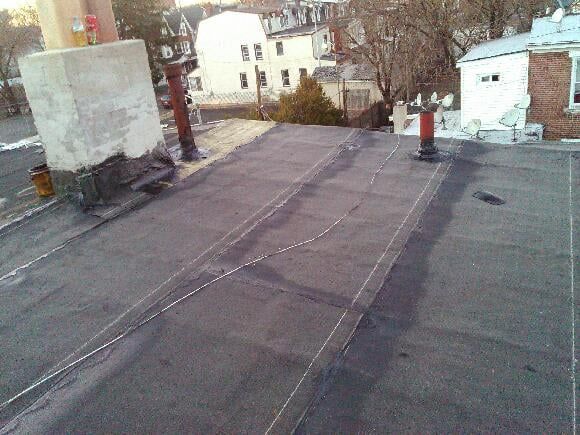 Flat rooftop with vents and skylights overlooking houses and leafless trees