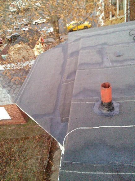 Roof with gray shingles and an orange vent pipe, viewed from above amid autumn trees