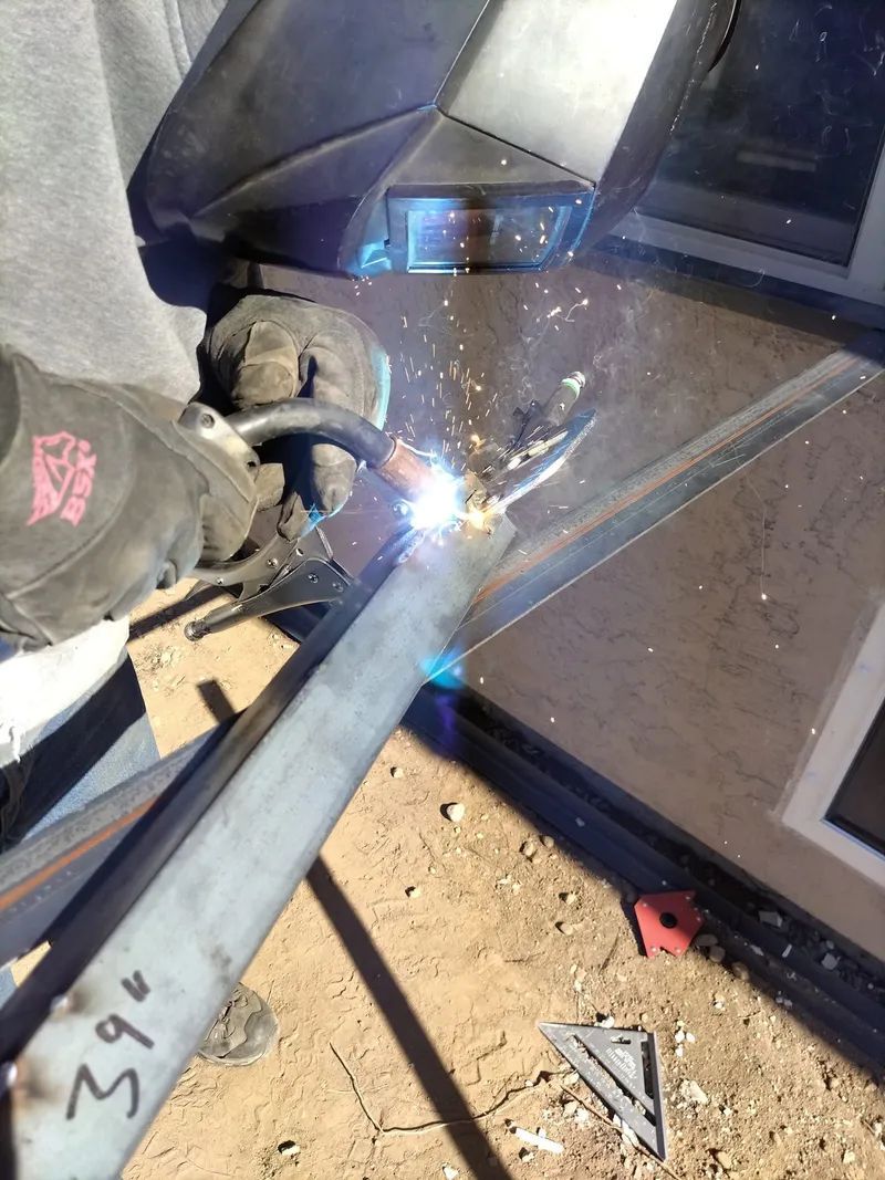 Welder joining a metal frame, bright sparks in a windowed industrial area
