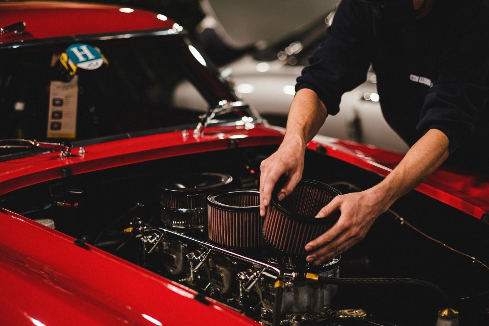 Hands working on a car engine in a red classic car garage