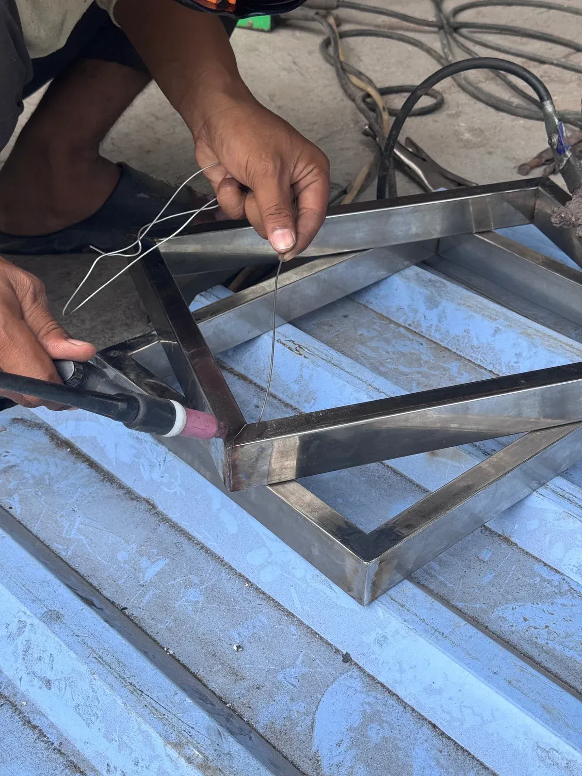 Hands welding a metal frame on a corrugated roof with a power tool and tangled cables nearby