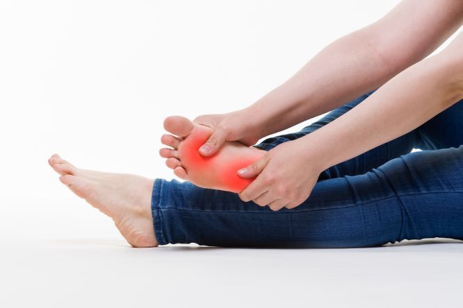 A Woman Is Sitting On The Floor Holding Her Foot In Pain — Physiocare In Buderim, QLD