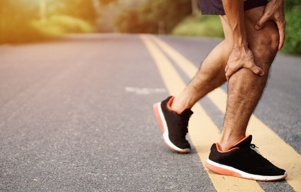 A Man Is Holding His Knee In Pain While Walking Down The Road — Physiocare In Buderim, QLD