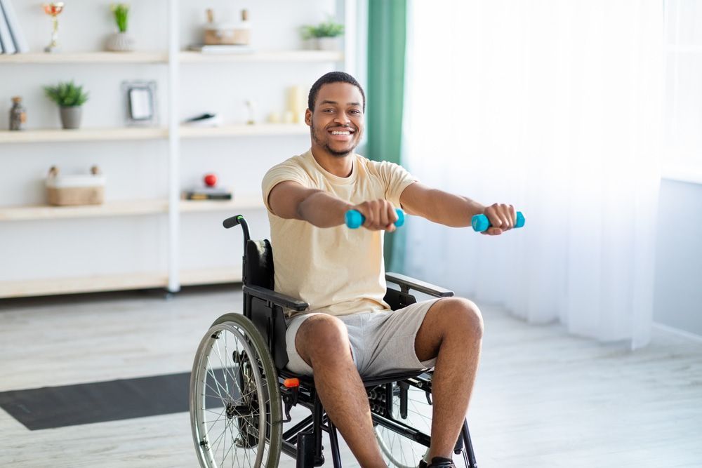 A Man In A Wheelchair Is Lifting Dumbbells — Physiocare In Mooloolaba, QLD