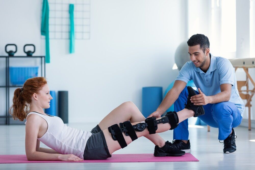A Man Is Helping A Woman With A Knee Brace — Physiocare In Buderim, QLD