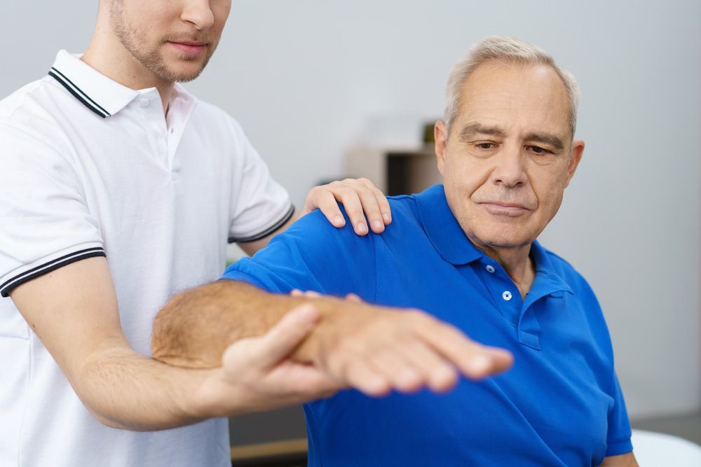 A Man In A Blue Shirt Is Being Helped By A Man In A White Shirt — Physiocare In Mooloolaba, QLD