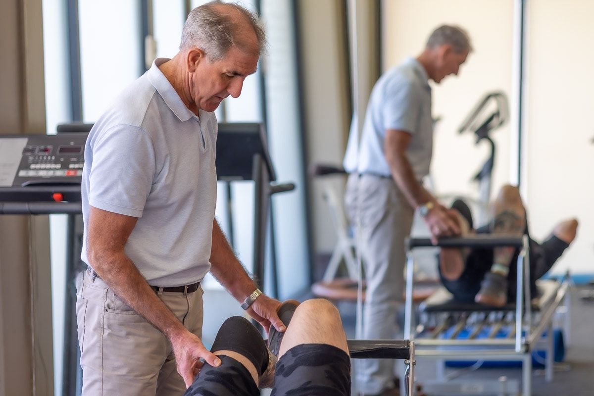 A Man Is Examining A Patient 's Knee In A Gym — Physiocare In Buderim, QLD