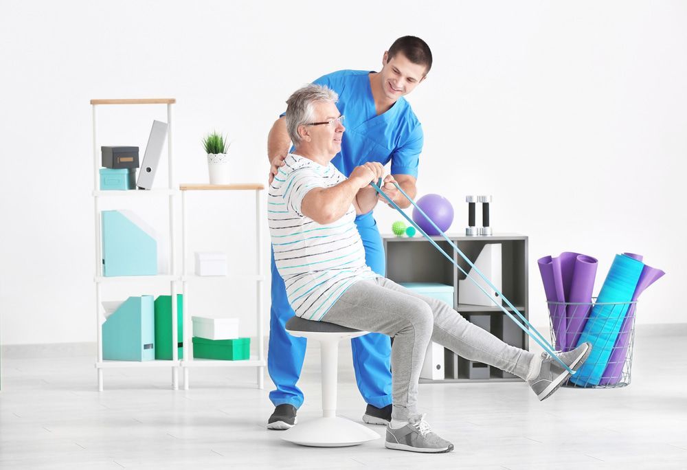 A Nurse Is Helping An Elderly Man Do Exercises With A Resistance Band — Physiocare In Mooloolaba, QLD