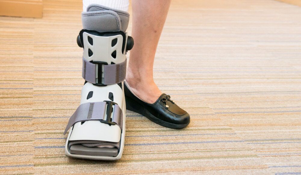 A Person Wearing A Walking Boot And Black Shoes Is Standing On A Carpeted Floor — Physiocare In Mooloolaba, QLD