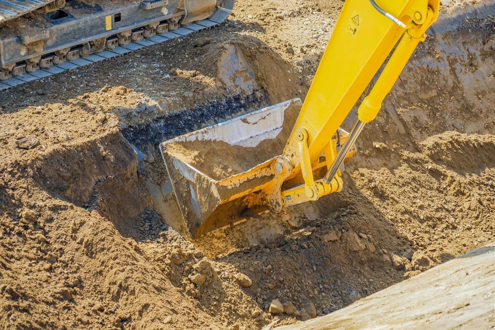 Yellow excavator digging dirt in a construction trench