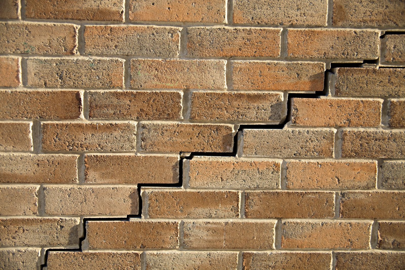 Brick wall with a jagged stair-step crack running diagonally across it